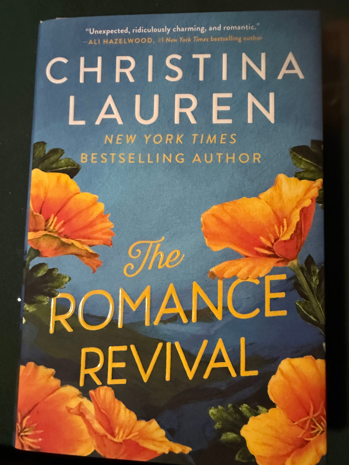 The front cover of the book 'The Romance Revival' by Christina Lauren, featuring a blue background with large orange flowers and gold lettering.