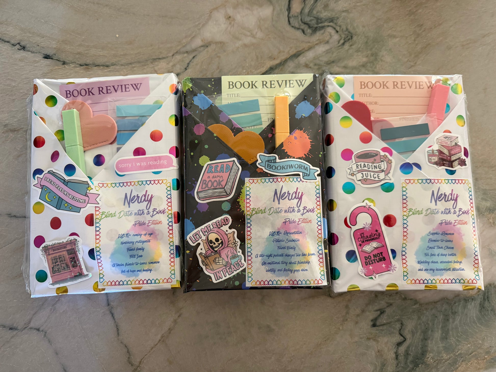 Three packaged book review cards or mini booklets arranged side by side on a gray marble surface. The designs are colorful and themed with school and book motifs, including polka dots, sticky notes, and book illustrations.