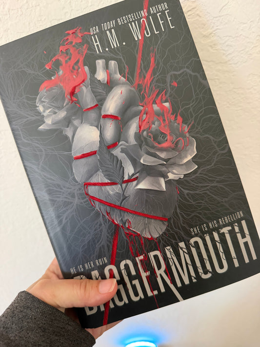 A hand holding a book titled 'Daggermouth' by H.M.