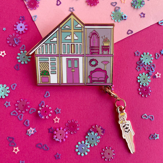 Colorful dollhouse-shaped keychain with a character charm on a pink background with decorative elements.