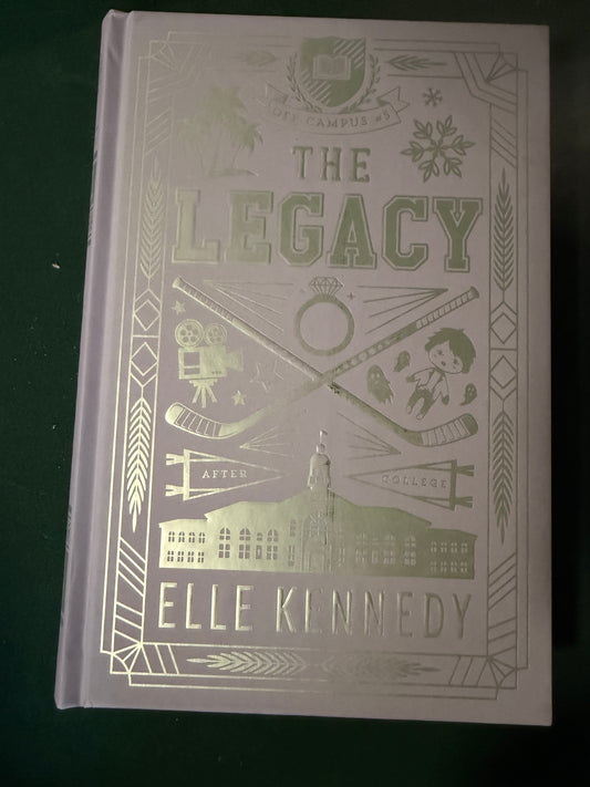 The Legacy hardcover book by Elle Kennedy, featuring a pale lavender cover with metallic gold foil illustrations and text, photographed on a dark green background.